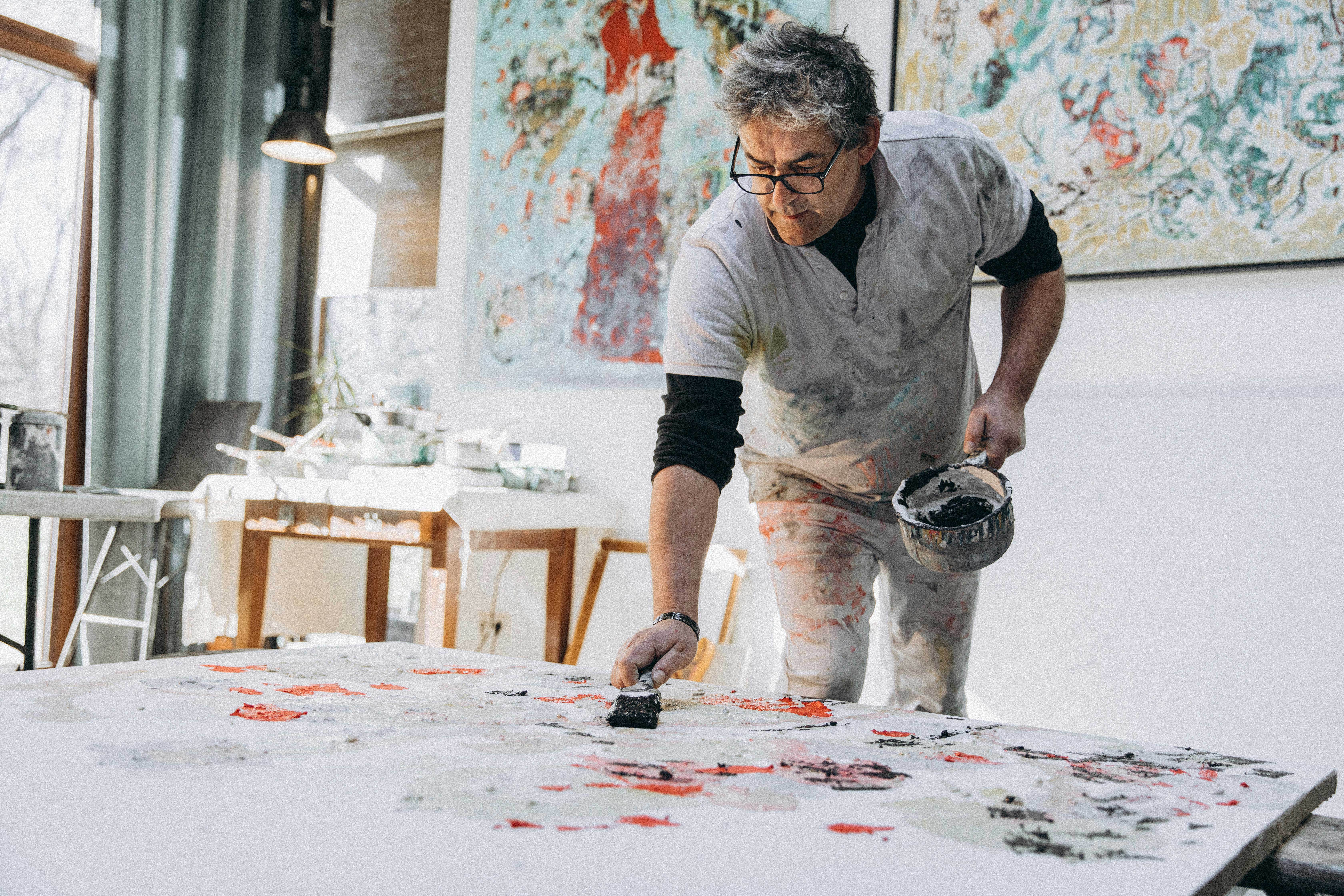 Older man painting on a floor canvas